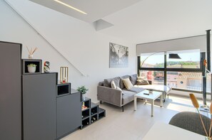 A modern living room with a grey sofa, a white coffee table, and a large window offering a city view. - GRAN RESERVA MIMOSES ATIC B (Empuriabrava)