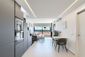 A modern kitchen with a dining area, large windows, and a view of buildings. - GRAN RESERVA MIMOSES ATIC B (Empuriabrava)