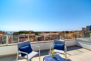 A rooftop terrace with two blue chairs, a table, and a bottle of wine. - GRAN RESERVA MIMOSES ATIC B (Empuriabrava)