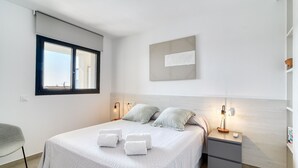 A bedroom with a bed, pillows, a nightstand, a lamp, a window, and a wall-mounted artwork. - GRAN RESERVA MIMOSES ATIC B (Empuriabrava)