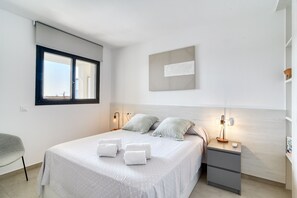 A bedroom with a bed, pillows, a nightstand, a lamp, a window, and a wall-mounted artwork. - GRAN RESERVA MIMOSES ATIC B (Empuriabrava)