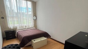 Un dormitorio con cama, mesita de noche, cómoda, taburete pequeño y escritorio.