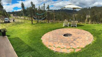 A backyard with a stone fire pit, a hammock, and two lawn chairs.