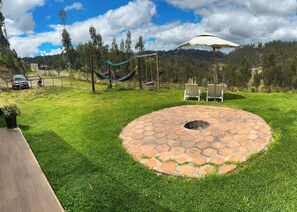Un patio trasero con un pozo de fuego de piedra, una hamaca y dos sillas de jardín.