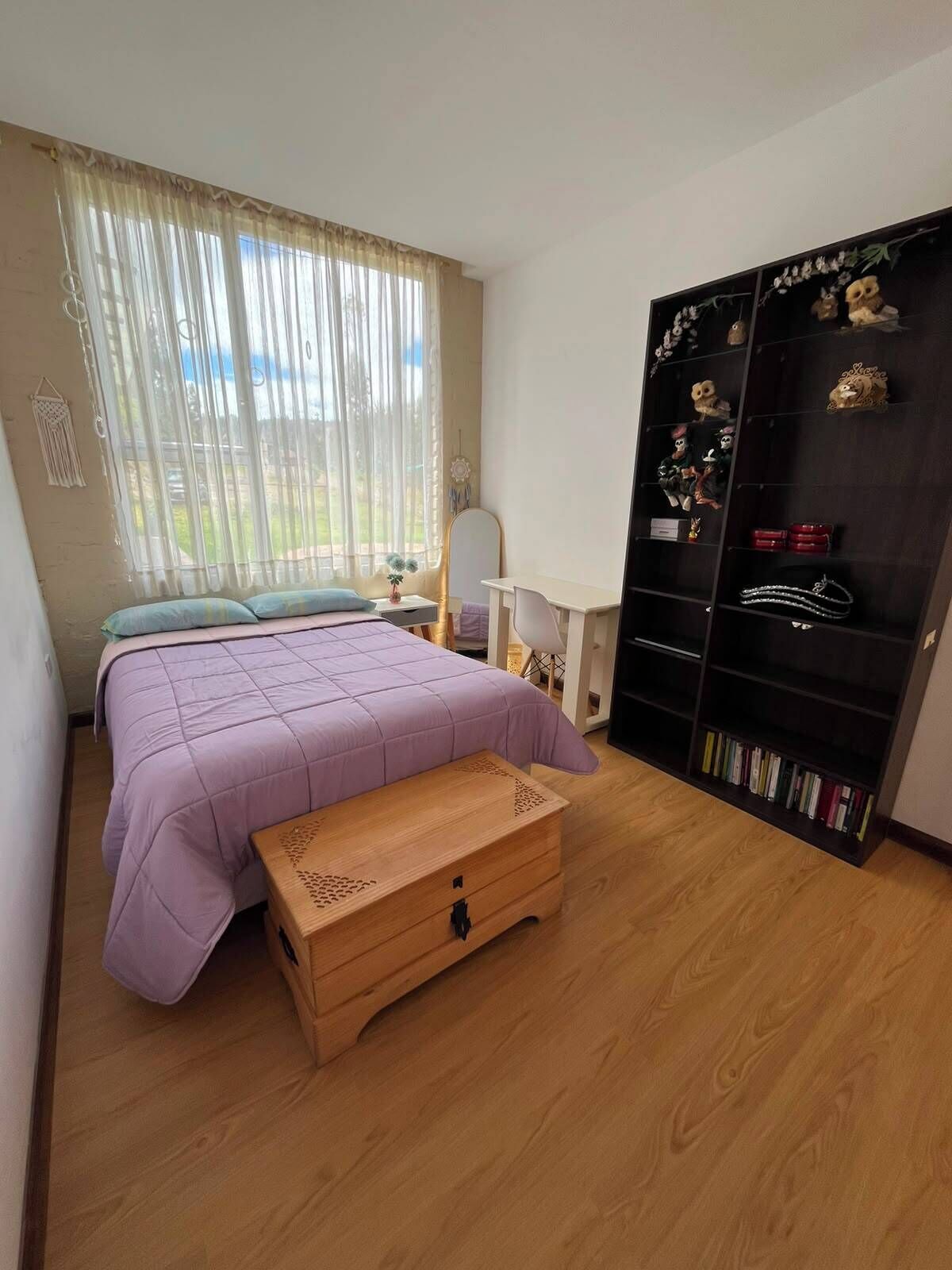 A bedroom with a bed, a wooden chest, a desk, and a bookshelf.