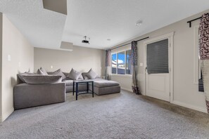 Ein Wohnzimmer mit einer Eckcouch, einem kleinen Tisch und einem großen Fenster mit Vorhängen.