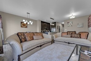 A living room with two sofas, a coffee table, and a kitchen in the background. - Stylish 4BR Walkout | Theatre Room | Pond Views | Near Airport (Edmonton)