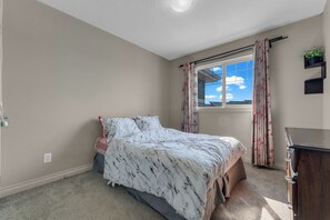 A bedroom with a bed, a window, a dresser, and a small plant on a shelf. - Stylish 4BR Walkout | Theatre Room | Pond Views | Near Airport (Edmonton)