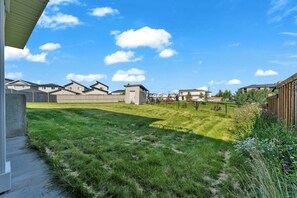 A residential area with houses, a grassy yard, and a clear sky. - Stylish 4BR Walkout | Theatre Room | Pond Views | Near Airport (Edmonton)