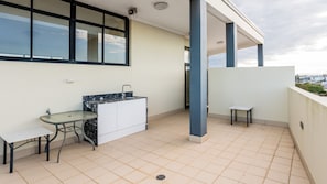 A balcony with a kitchen area, including a sink, a table, and a chair.