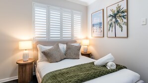 Ein ordentlich gemachtes Bett mit einer grünen Decke, zwei Nachttischlampen und zwei gerahmten Bildern an der Wand.