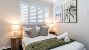 Ein ordentlich gemachtes Bett mit einer grünen Decke, zwei Nachttischlampen und zwei gerahmten Bildern an der Wand.