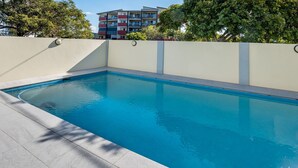 Ein rechteckiger Swimmingpool mit einer Fliesenleiste, umgeben von einer niedrigen Mauer und einem gefliesten Boden.