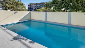 Ein rechteckiger Swimmingpool mit einer Fliesenleiste, umgeben von einer niedrigen Mauer und einem gefliesten Boden.