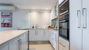 A modern kitchen with white cabinetry, stainless steel appliances, and a large window.