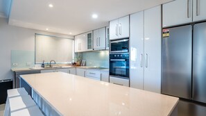 A modern kitchen with a central island, stainless steel appliances, and light-colored cabinetry. - The Peninsula Hideaway Pool & Walk to Suttons Beach (Redcliffe)