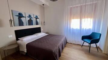 Une chambre d’hôtel avec un lit, une chaise, un tableau au mur et une fenêtre avec des rideaux.