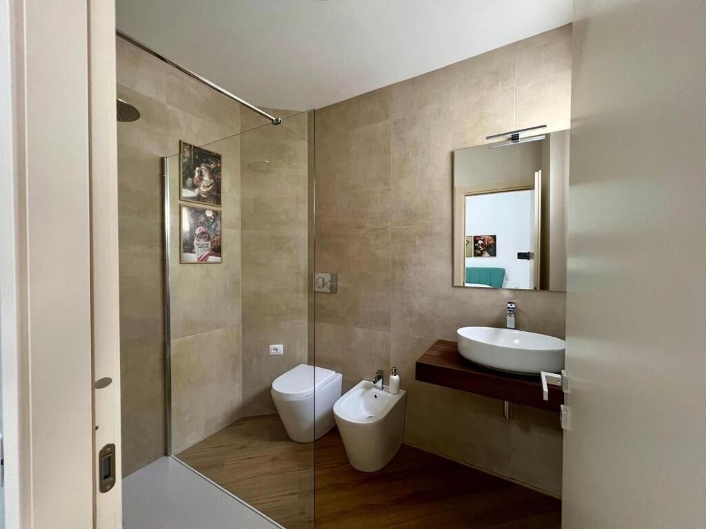A modern bathroom with a glass shower enclosure, a toilet, a bidet, and a sink with a mirror above it.