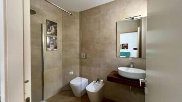 A modern bathroom with a glass shower enclosure, a toilet, a bidet, and a sink with a mirror above it.