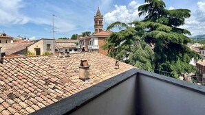 Una terraza en la azotea con tejas de terracota, una torre campanario y edificios circundantes.