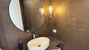Un baño moderno con un espejo redondo, un lavamanos blanco y dos luces empotradas.