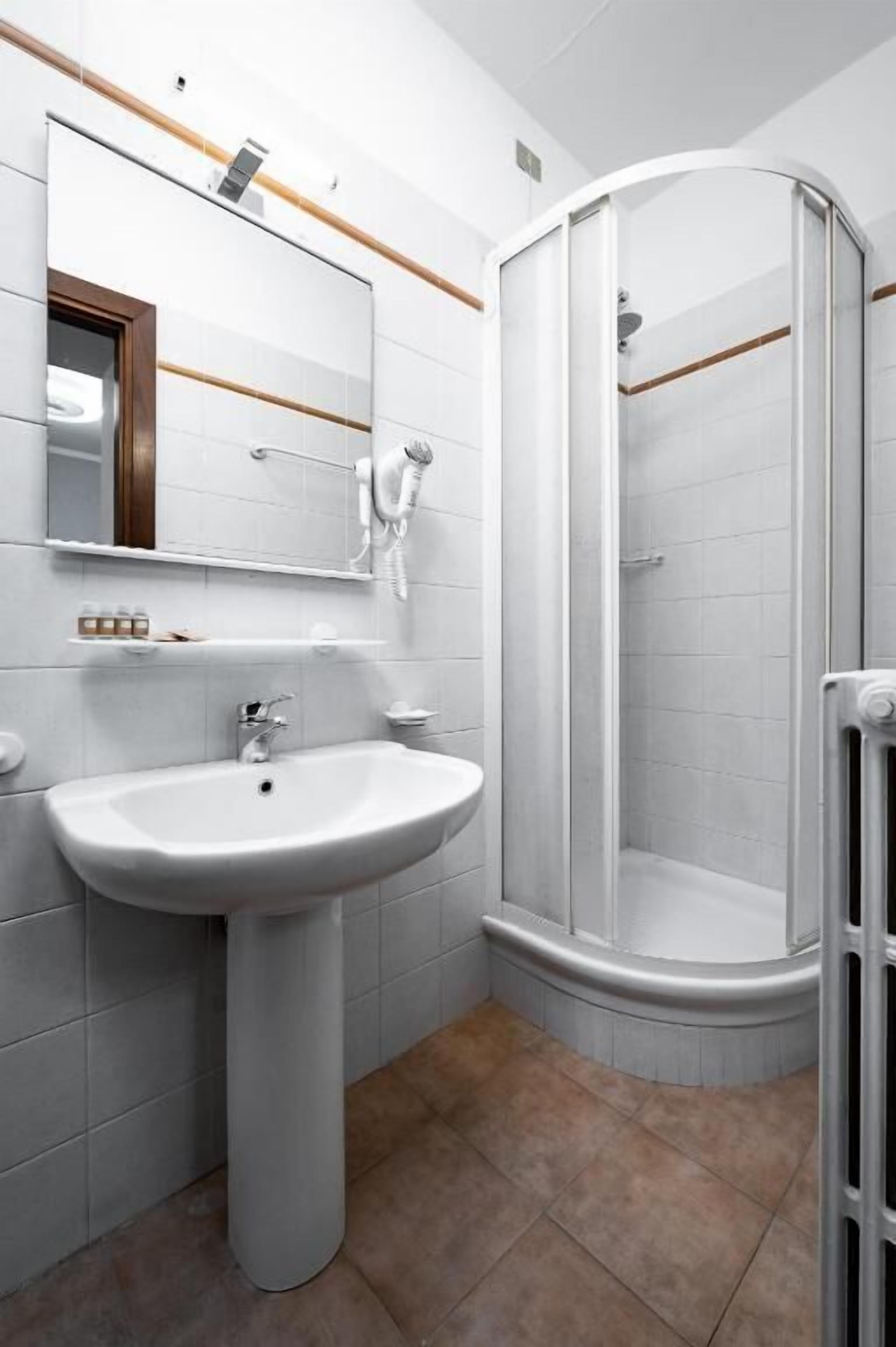Un bagno moderno con un lavabo su piedistallo, una cabina doccia in vetro e uno specchio con cornice in legno.