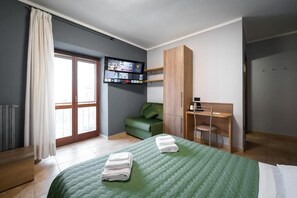 Quarto de hotel com cama, escrivaninha, cadeira, televisão e guarda-roupa.