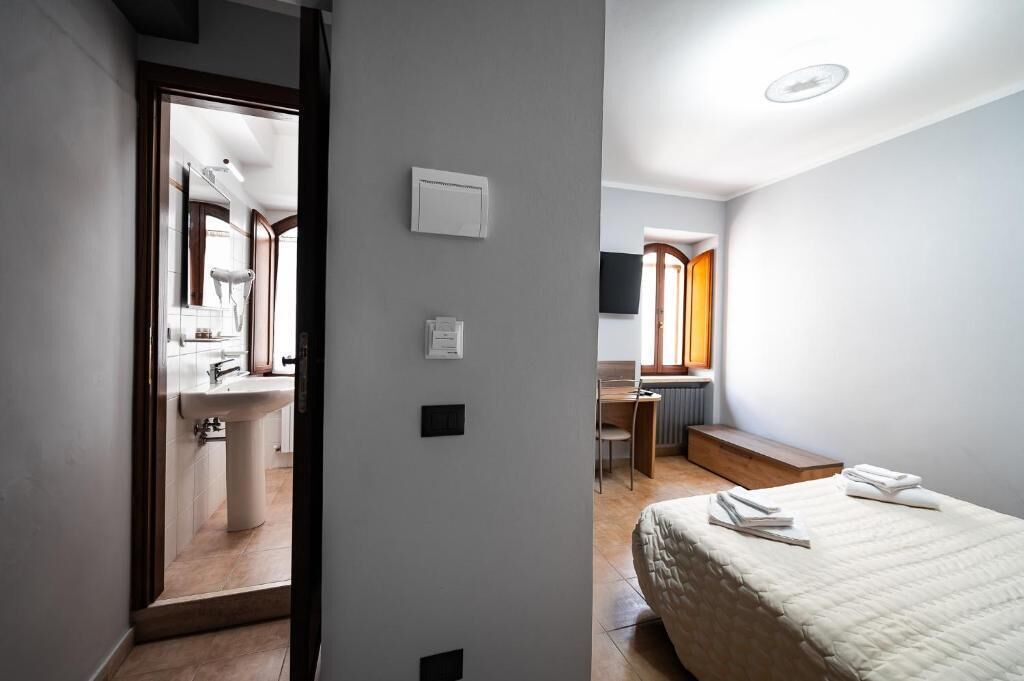 A hotel room with a bed, a desk, a chair, a window, and a bathroom visible through an open door.