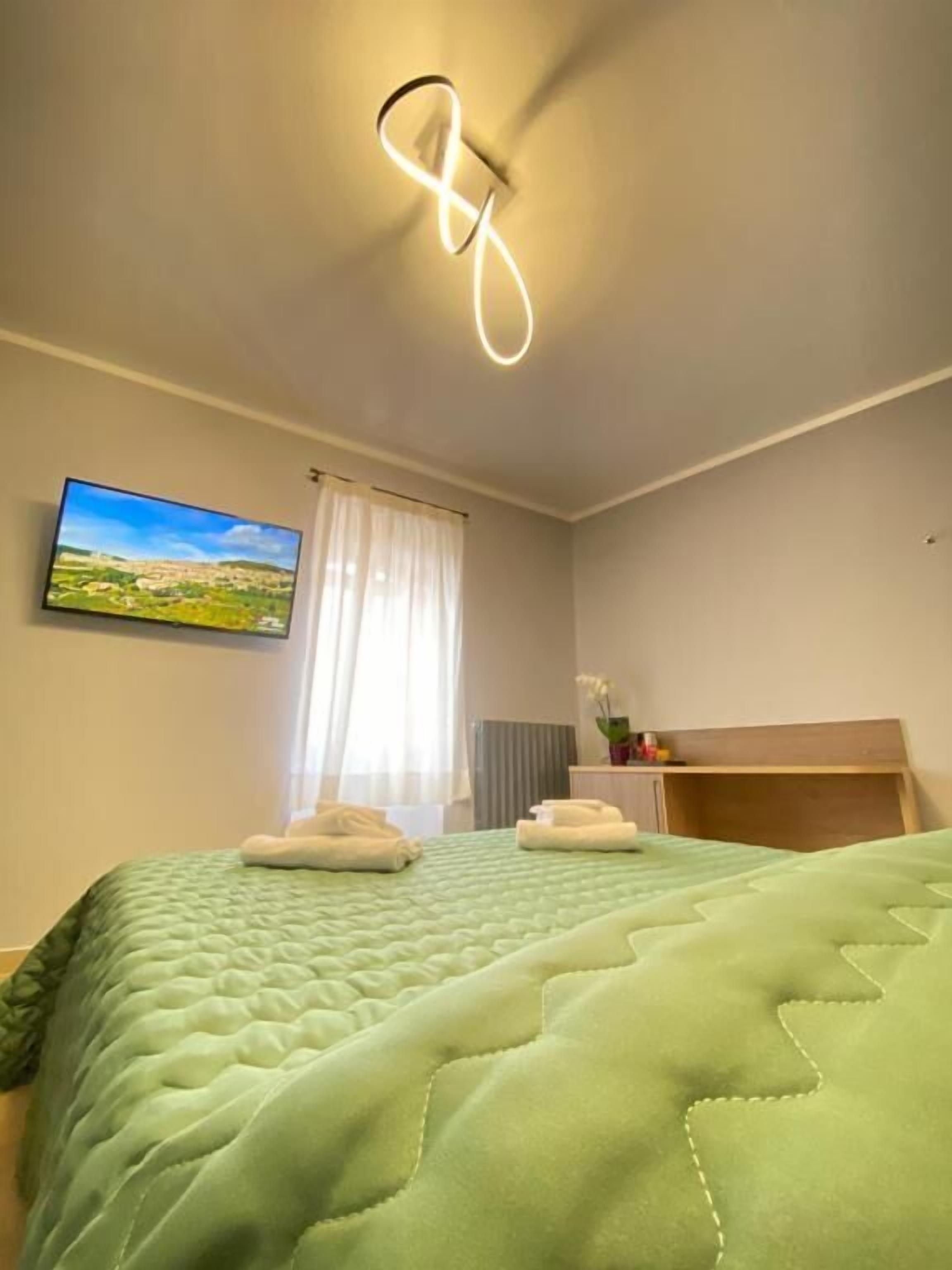 Ein Hotelzimmer mit einem Bett, einem Fernseher, einem Fenster mit Vorhängen und einem Nachttisch mit einer Vase.