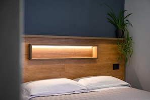 A bed with white bedding, a wooden headboard, and a wall-mounted light fixture.