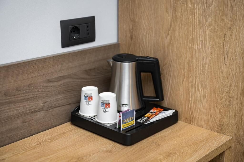 A coffee station with a kettle, two cups, and a tray with a coffee sachet.