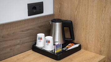 A coffee station with a kettle, two cups, and a tray with a coffee sachet.