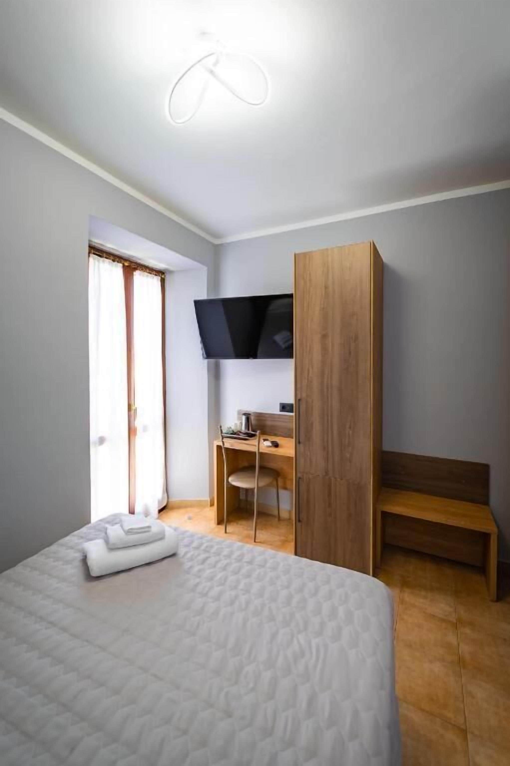 Een slaapkamer met een bed, een bureau, een stoel, een televisie en een houten garderobe.