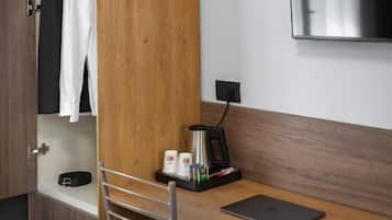 Ein Hotelzimmer mit einem Holztisch, einem Sessel, einem Bett, einem an der Wand befestigten Fernseher und einem Kleiderschrank.