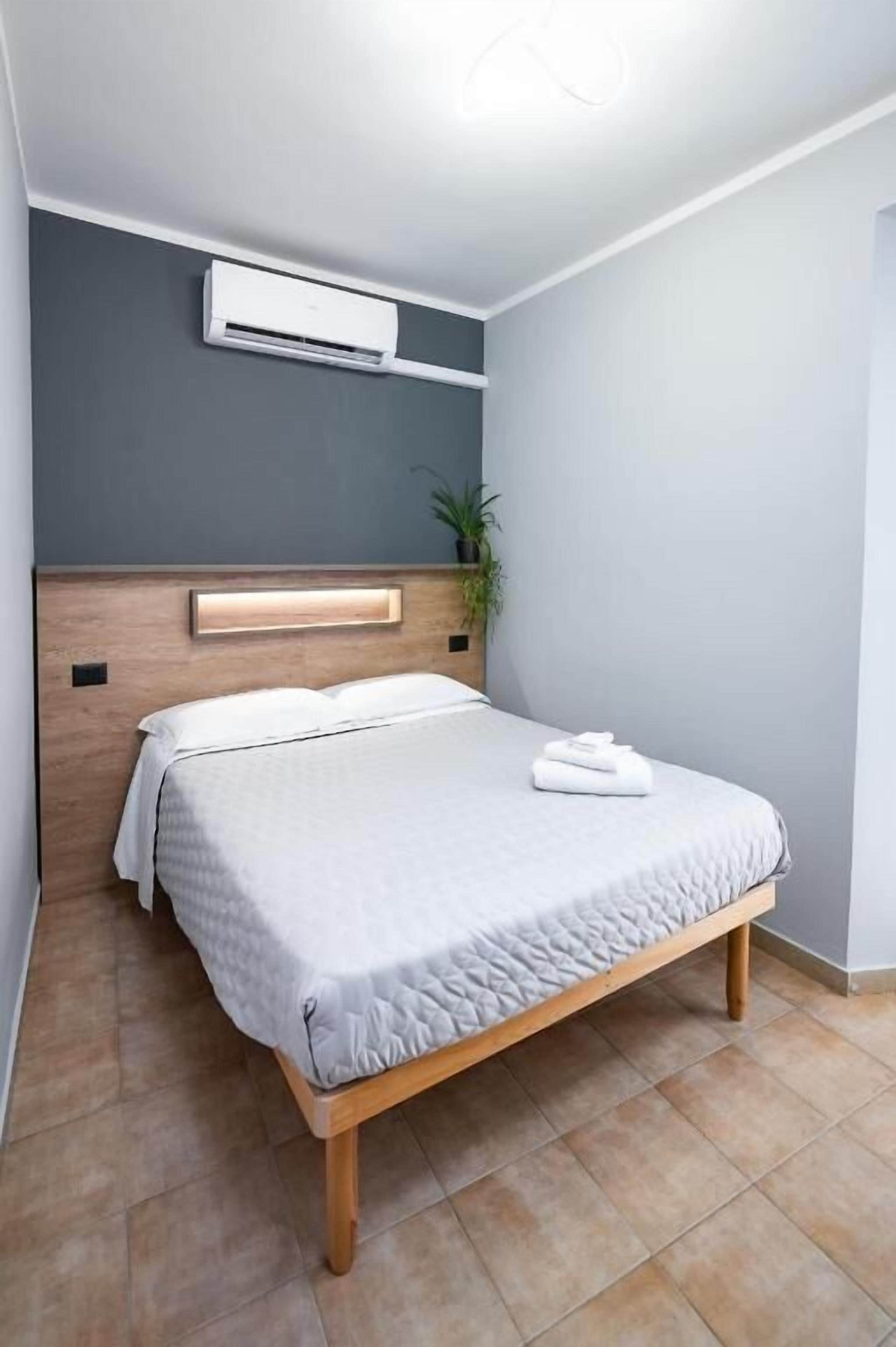 Une chambre à coucher moderne avec un lit, un appareil de climatisation, une tête de lit et une plante en pot.