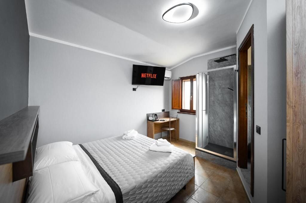 A modern bedroom with a bed, a desk, a shower, and a TV displaying Netflix.