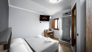 A modern bedroom with a bed, a desk, a shower, and a TV displaying Netflix.