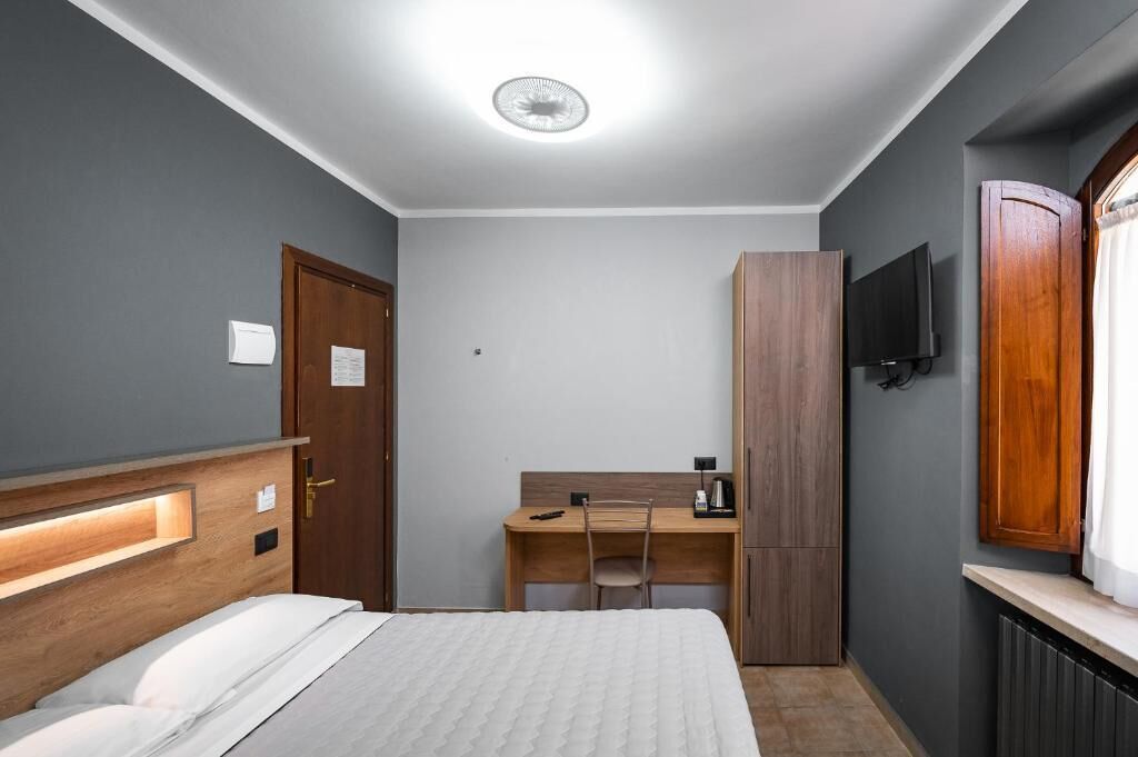 Habitación de hotel con cama, escritorio, armario, televisor y ventana.