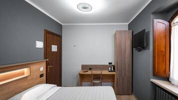 Habitación de hotel con cama, escritorio, armario, televisor y ventana.
