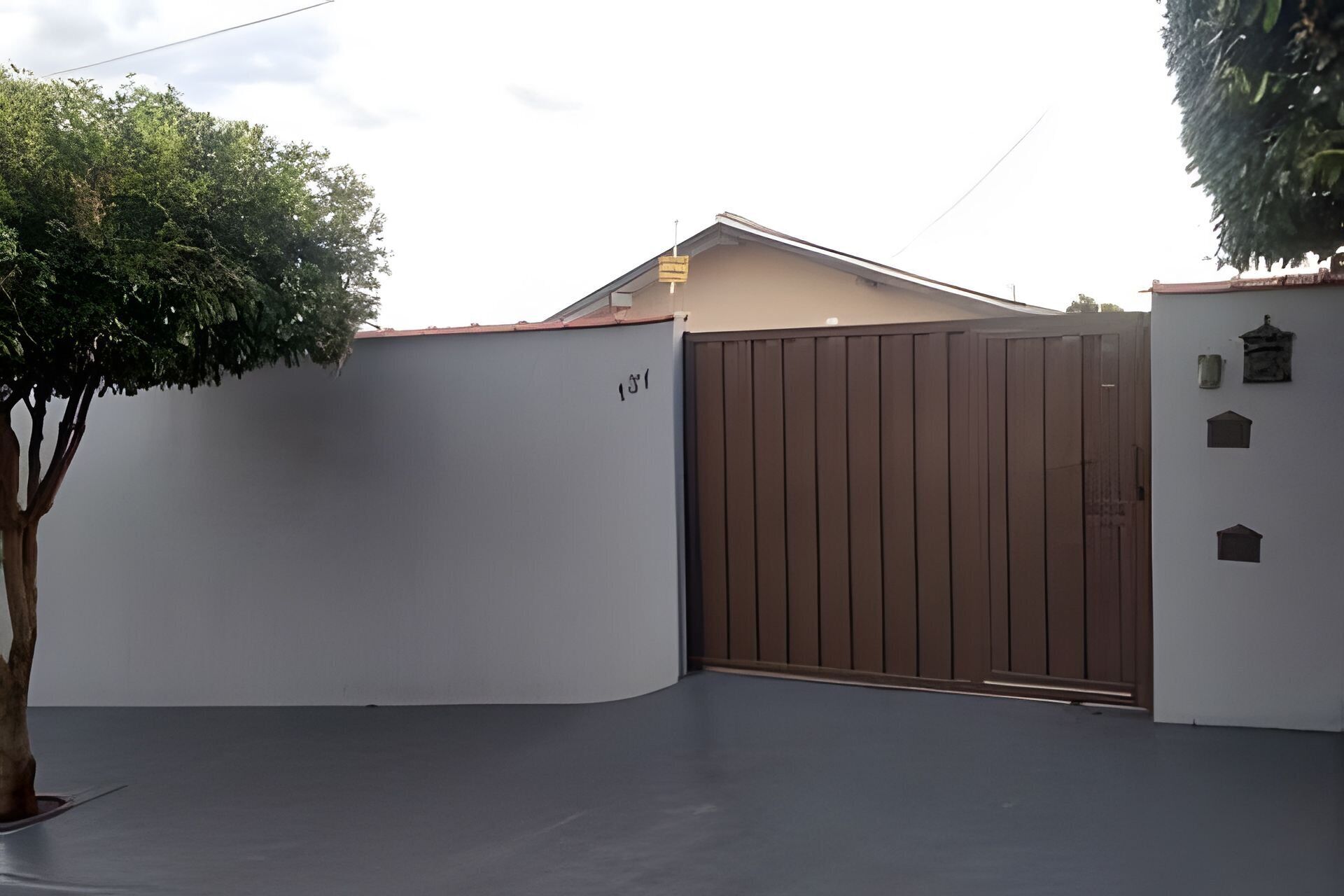 Una entrada con portón, un árbol y un edificio de techo plano.