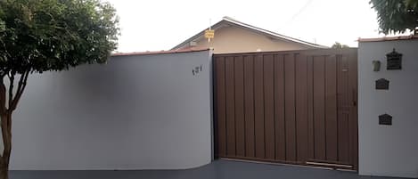 A gated entrance with a brown gate, a tree, and a building with a flat roof.