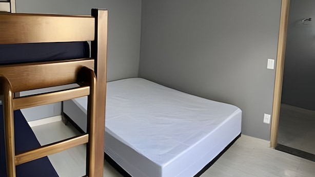 A small, single-bed room with a wooden bunk bed on one side and a plain mattress on the other.