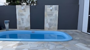A swimming pool with a stone tile deck, surrounded by a grey wall with a stone pattern.