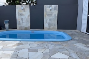 Una piscina con borde de baldosas de piedra, rodeada por un muro gris con diseño pétreo.