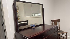 Un aparador de madera con un espejo, una silla y una ventana con persianas.