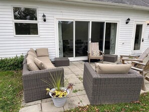 Eine Terrasse mit Korbmöbeln, einem Blumentopf und einer Schiebetür zu einem überdachten Bereich.