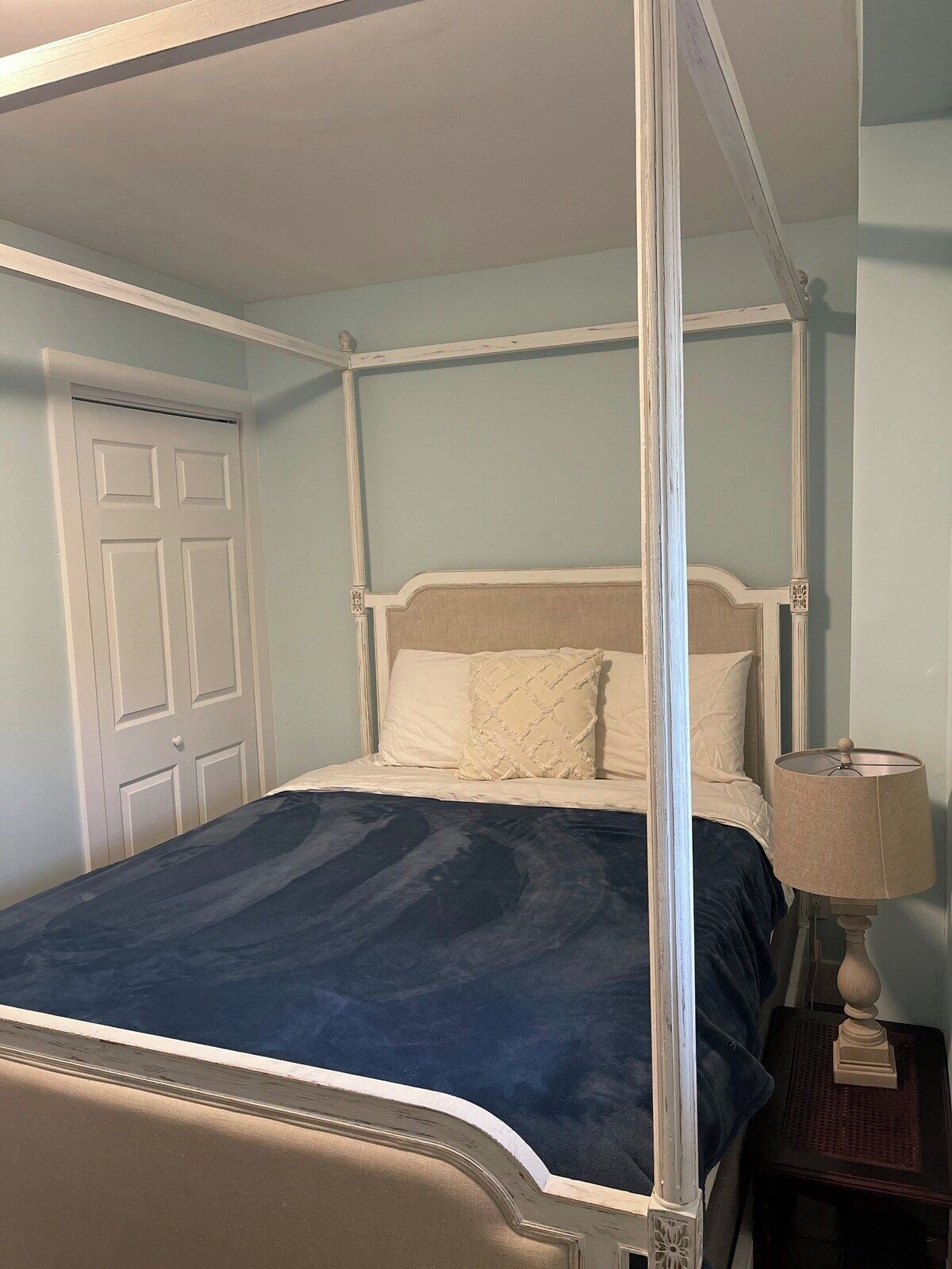 A four-poster bed with a dark blue bedspread, a white headboard, and two pillows.