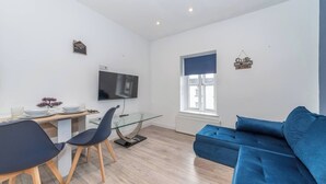 A modern living room with a sofa, a dining table with chairs, a TV, and a window with a view. - Ibex House Cozy Modern 2-bed Flat Free Parking (Reading)