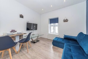 Ein modernes Wohnzimmer mit Sofa, Esstisch mit Stühlen, Fernseher und Fenster mit Blick.