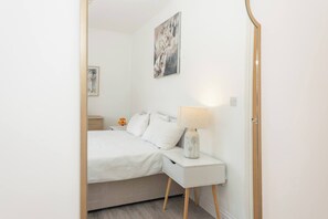 A bedroom with a bed, bedside table, lamp, and a wall-mounted picture. - Ibex House Cozy Modern 2-bed Flat Free Parking (Reading)